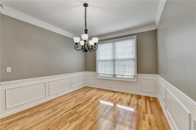 empty room with wainscoting, ornamental molding, a notable chandelier, and light wood-style flooring