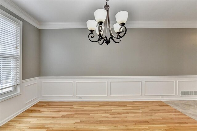 unfurnished dining area featuring light wood-type flooring, a wainscoted wall, a chandelier, and ornamental molding