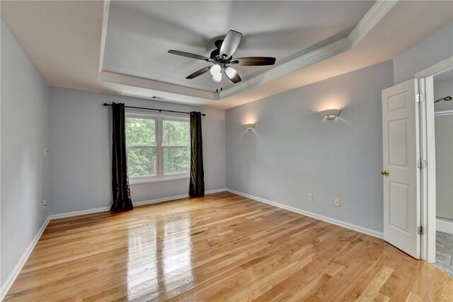 unfurnished room with a ceiling fan, baseboards, light wood-style floors, and a raised ceiling