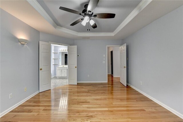unfurnished bedroom with light wood finished floors, a tray ceiling, ensuite bathroom, baseboards, and crown molding
