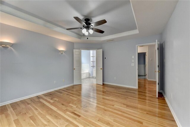 unfurnished bedroom featuring a raised ceiling, light wood-style flooring, and baseboards