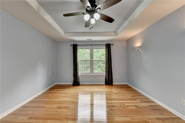 unfurnished room featuring baseboards, a ceiling fan, light wood finished floors, and a raised ceiling