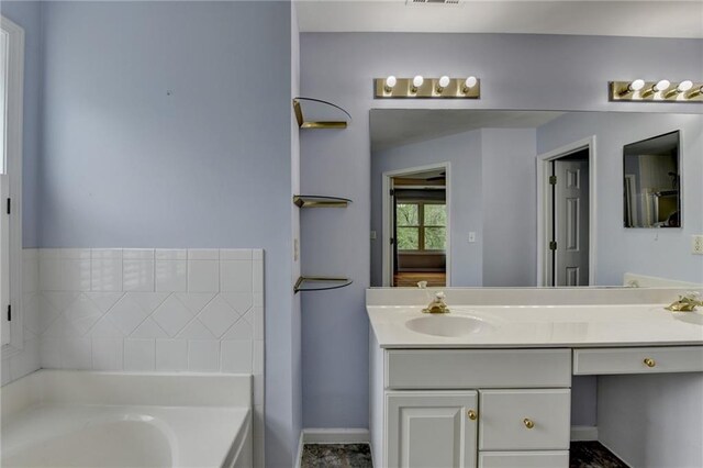 bathroom with a garden tub, vanity, visible vents, and baseboards