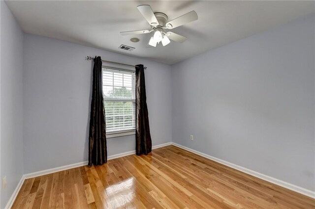 unfurnished room with light wood-type flooring, visible vents, a ceiling fan, and baseboards