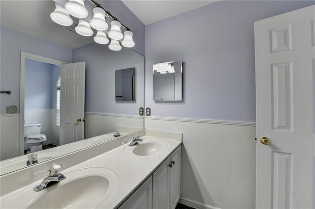 full bath featuring toilet, a wainscoted wall, a sink, and double vanity
