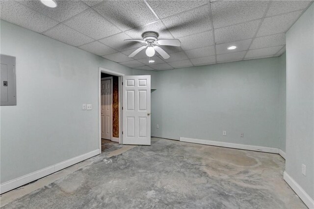 empty room featuring a ceiling fan, concrete flooring, a drop ceiling, electric panel, and baseboards