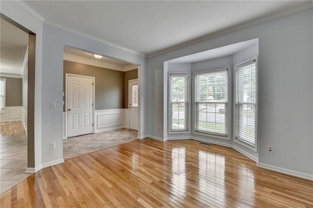 empty room featuring light wood-style flooring, visible vents, ornamental molding, and wainscoting