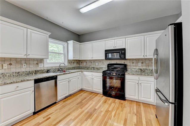 kitchen with white cabinets, a sink, light wood-style floors, decorative backsplash, and black appliances