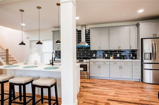 kitchen featuring sink, gray cabinetry, decorative light fixtures, appliances with stainless steel finishes, and wall chimney range hood