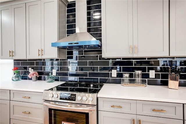 kitchen with gray cabinetry, backsplash, wall chimney exhaust hood, and stainless steel electric range oven