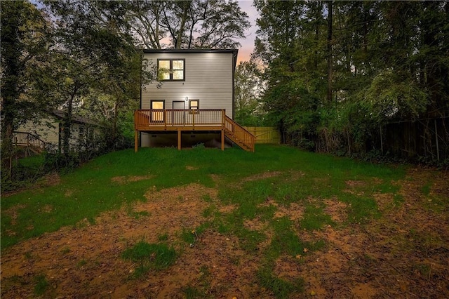 back house at dusk with a deck and a lawn