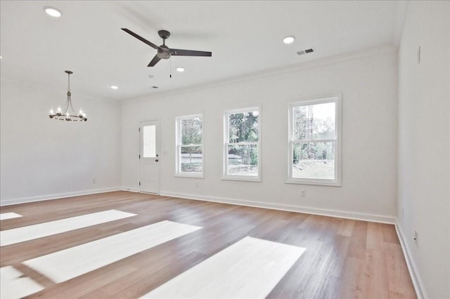 spare room with light wood finished floors, crown molding, ceiling fan with notable chandelier, and visible vents