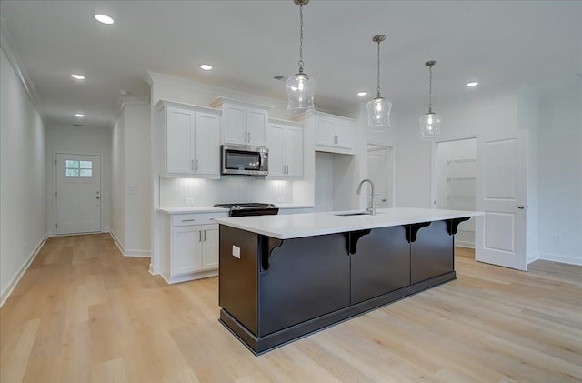 kitchen with stainless steel microwave, a sink, light wood-type flooring, a kitchen bar, and baseboards