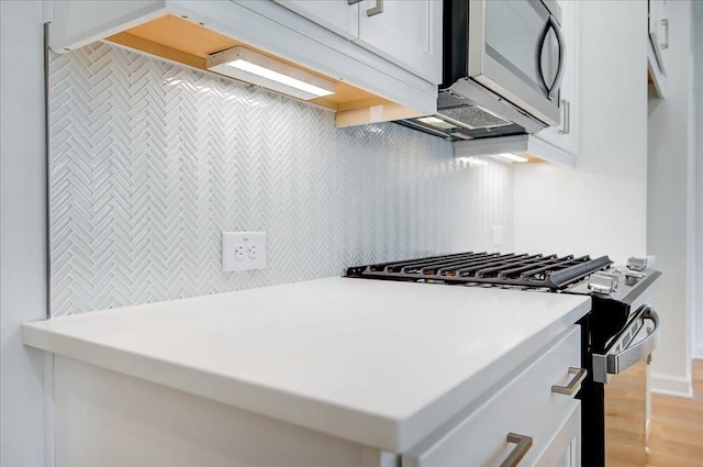 kitchen with light wood-style flooring, white cabinetry, backsplash, light countertops, and appliances with stainless steel finishes