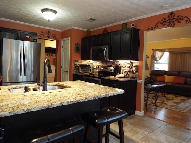 kitchen featuring appliances with stainless steel finishes, sink, a kitchen bar, light stone counters, and crown molding