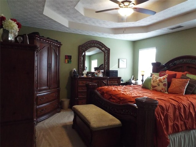 bedroom with ceiling fan, a tray ceiling, light colored carpet, and a textured ceiling