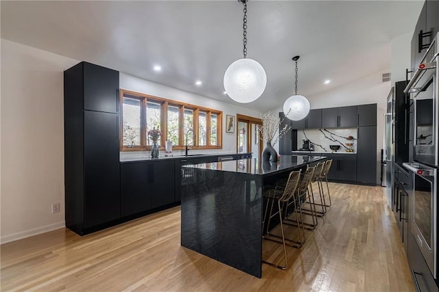 kitchen with light wood-type flooring, sink, decorative light fixtures, a center island, and lofted ceiling