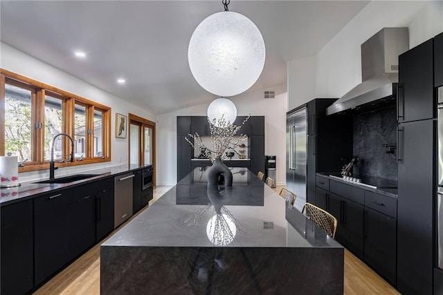 kitchen featuring appliances with stainless steel finishes, sink, wall chimney range hood, decorative light fixtures, and a large island