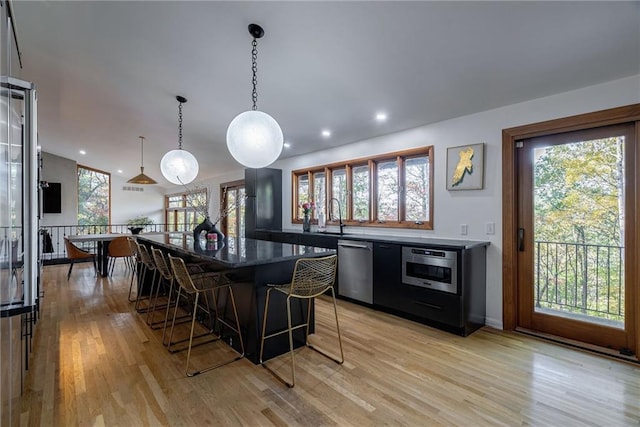 kitchen with decorative light fixtures, light wood-type flooring, stainless steel appliances, and a wealth of natural light