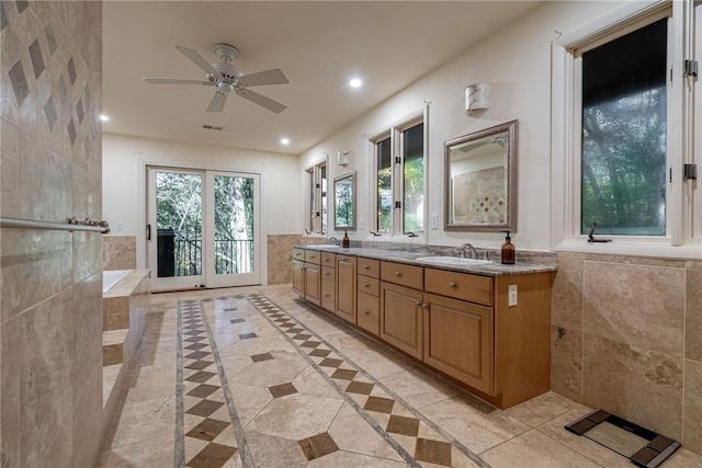 bathroom featuring a tub to relax in, ceiling fan, vanity, and tile walls