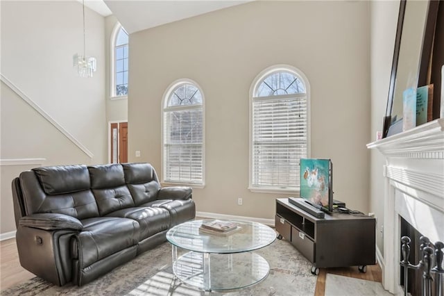 living room featuring a premium fireplace, light hardwood / wood-style flooring, a high ceiling, and a notable chandelier