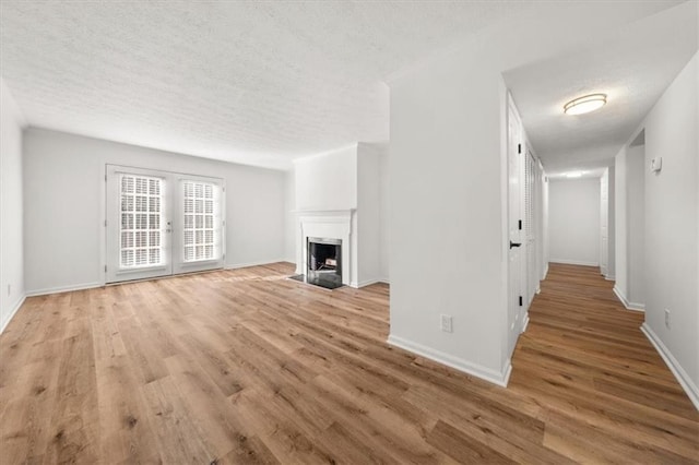 unfurnished living room featuring light hardwood / wood-style floors, french doors, and a textured ceiling