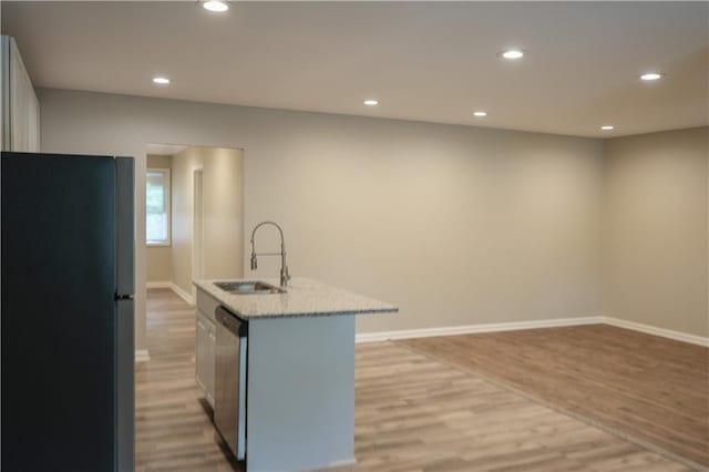 kitchen featuring a kitchen island with sink, dishwasher, black fridge, light wood-type flooring, and sink