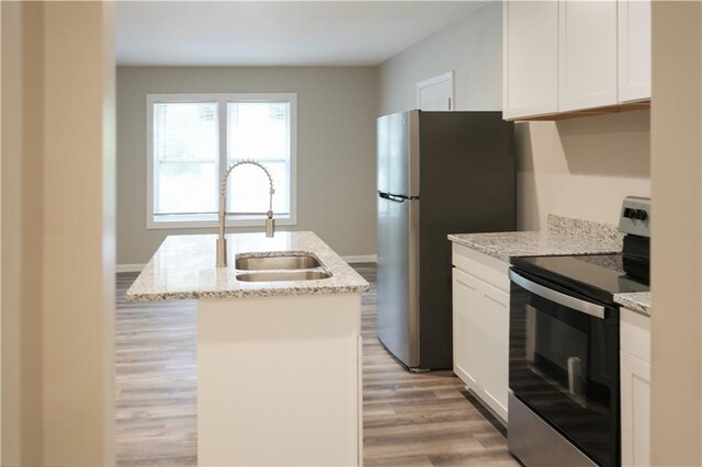 kitchen with light wood-type flooring, stainless steel appliances, an island with sink, light stone countertops, and sink