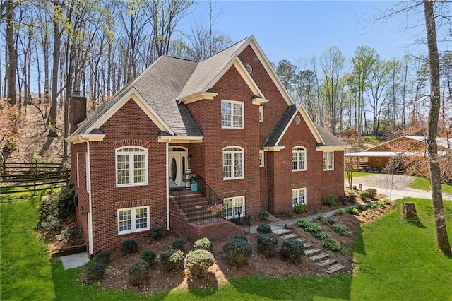 view of front of home with brick siding, a front lawn, fence, and a chimney