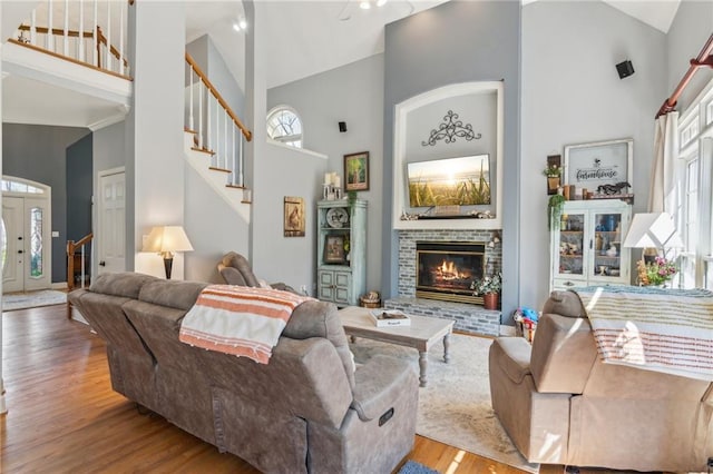 living area featuring stairs, a fireplace, high vaulted ceiling, and wood finished floors