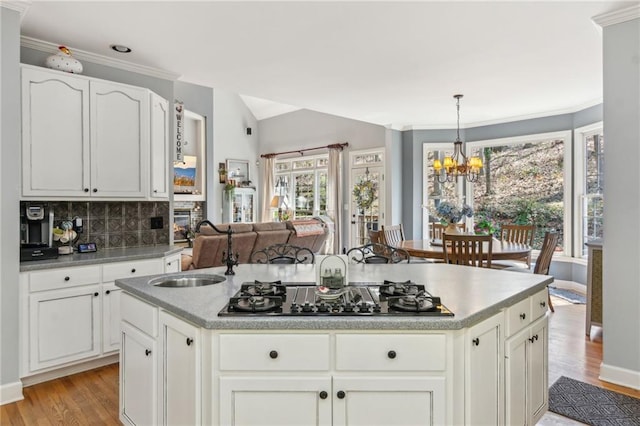 kitchen with black gas stovetop, a sink, light wood finished floors, a chandelier, and decorative backsplash