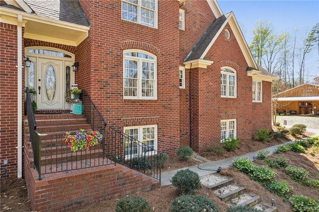 entrance to property featuring brick siding and roof with shingles