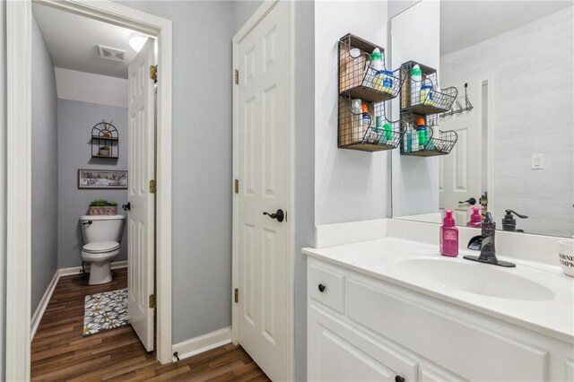bathroom featuring visible vents, baseboards, toilet, wood finished floors, and vanity