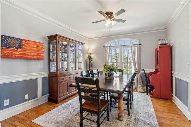 dining room featuring a wainscoted wall, light wood finished floors, crown molding, and a ceiling fan