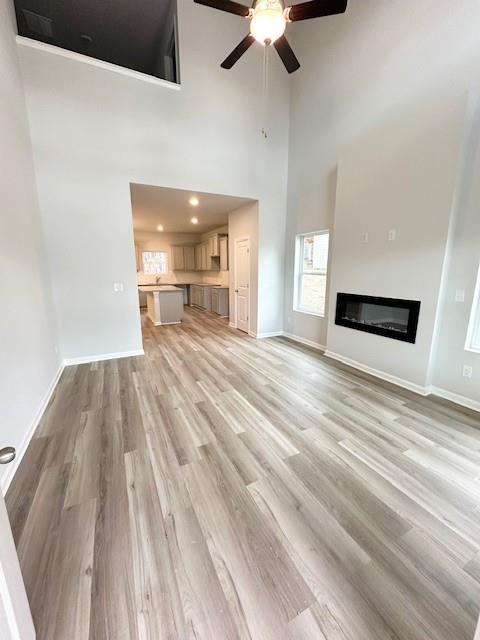 unfurnished living room with a high ceiling, ceiling fan, and light hardwood / wood-style flooring