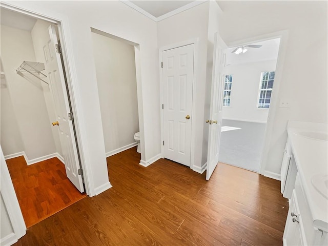 bathroom featuring baseboards, toilet, ornamental molding, wood finished floors, and vanity