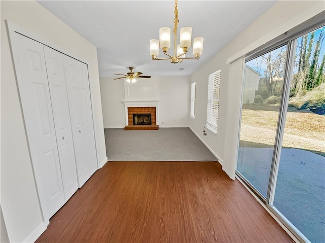 unfurnished living room with dark wood-style floors, a brick fireplace, baseboards, and ceiling fan with notable chandelier