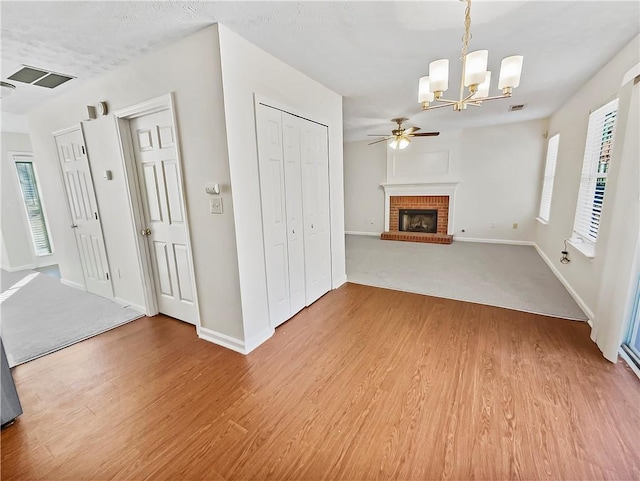 unfurnished living room featuring light wood-style floors, a brick fireplace, visible vents, and ceiling fan with notable chandelier