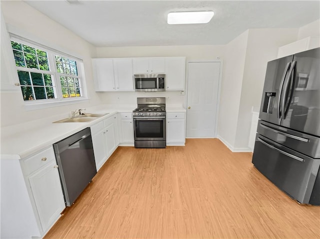 kitchen featuring stainless steel appliances, a sink, white cabinetry, light countertops, and light wood finished floors