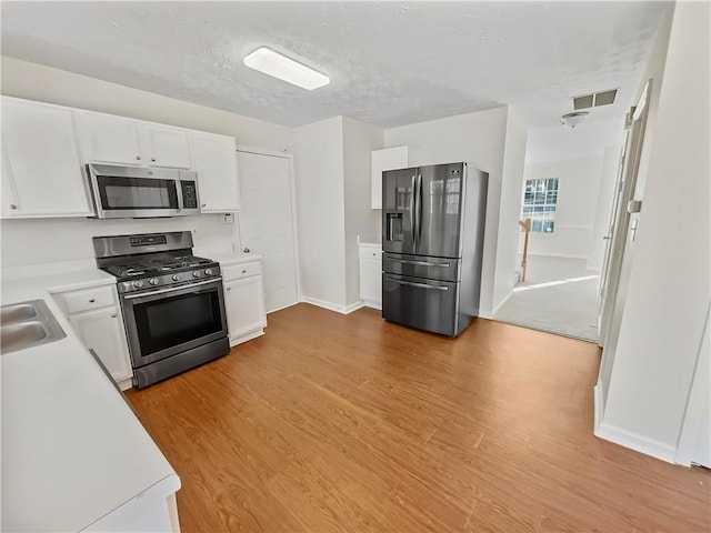 kitchen with a sink, white cabinetry, light countertops, appliances with stainless steel finishes, and light wood finished floors