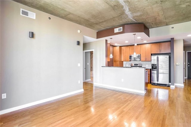 kitchen with appliances with stainless steel finishes, tasteful backsplash, sink, pendant lighting, and light hardwood / wood-style flooring