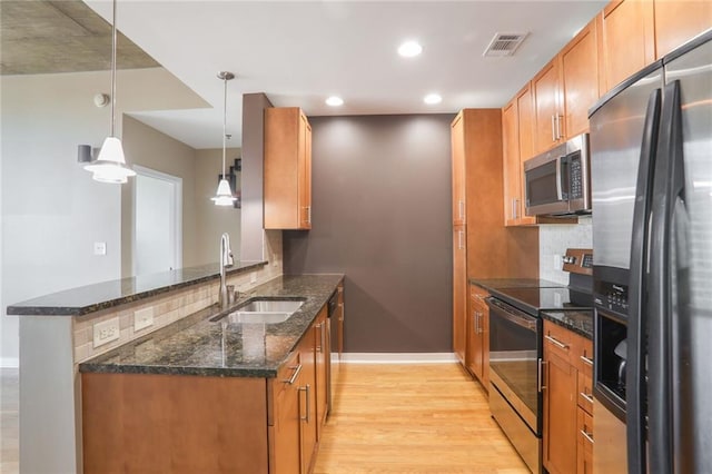 kitchen with light hardwood / wood-style flooring, hanging light fixtures, stainless steel appliances, sink, and dark stone countertops