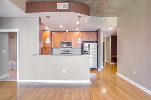 kitchen with decorative backsplash, appliances with stainless steel finishes, pendant lighting, dark stone countertops, and light hardwood / wood-style floors