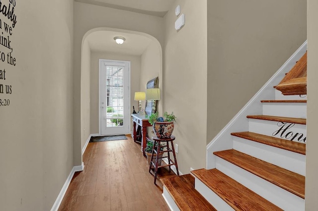 entryway featuring wood-type flooring, arched walkways, stairs, and baseboards
