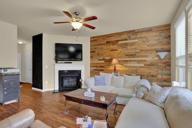 living room with wood finished floors, ceiling fan, a glass covered fireplace, baseboards, and wooden walls