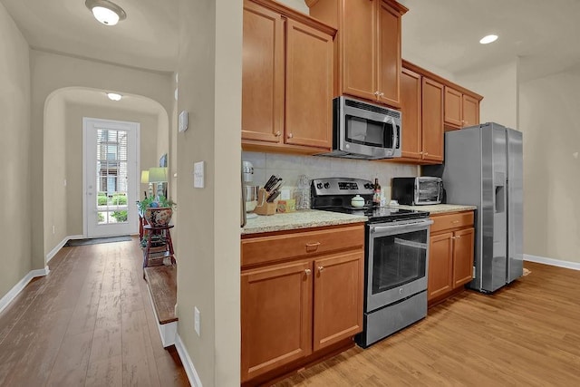 kitchen with stainless steel appliances, tasteful backsplash, light wood-style flooring, baseboards, and a toaster