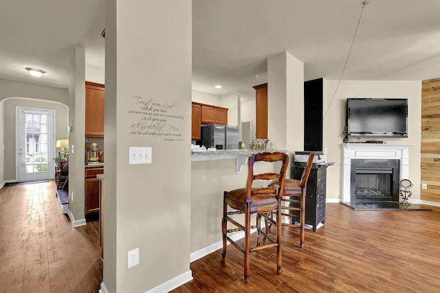 kitchen with brown cabinets, hardwood / wood-style floors, baseboards, a kitchen bar, and stainless steel refrigerator with ice dispenser