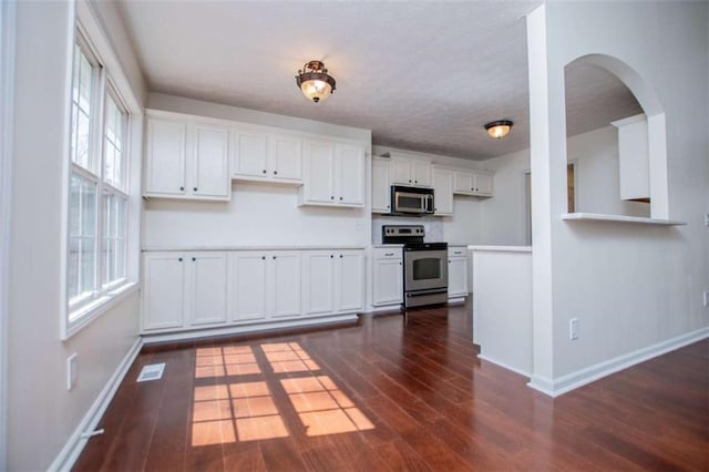 kitchen with white cabinetry, stainless steel appliances, dark wood-type flooring, and baseboards