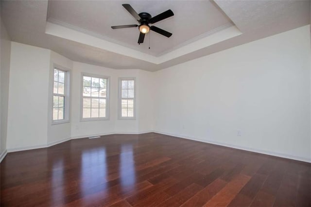 spare room with crown molding, a raised ceiling, baseboards, and wood finished floors