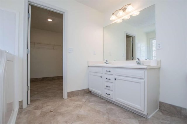 bathroom featuring baseboards, double vanity, a sink, a spacious closet, and tile patterned floors